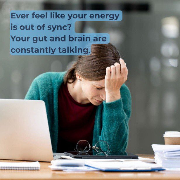 A stressed woman sitting at a desk with a laptop, holding her hand to her head in frustration, next to a light blue text overlay that reads: "Ever feel like your energy is out of sync? Your gut and brain are constantly talking."